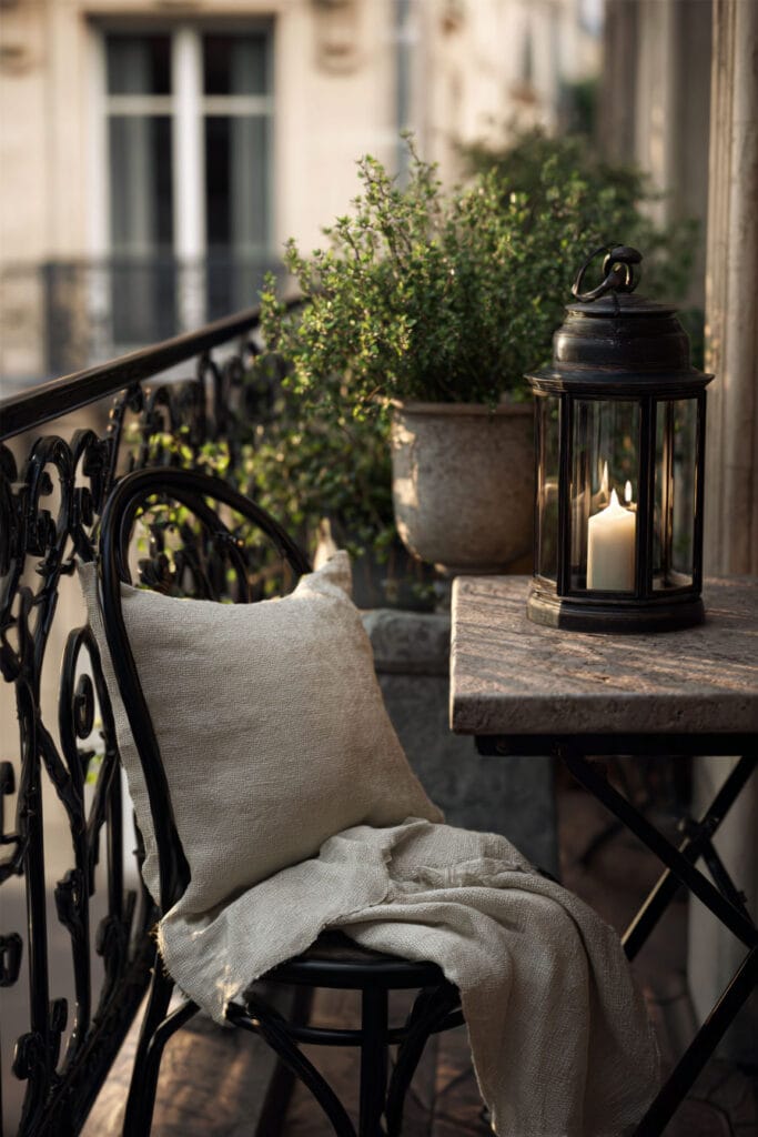 Paris balcony with wrought iron chair, lantern candle, linen throw, stone table, and cozy hidden café decor