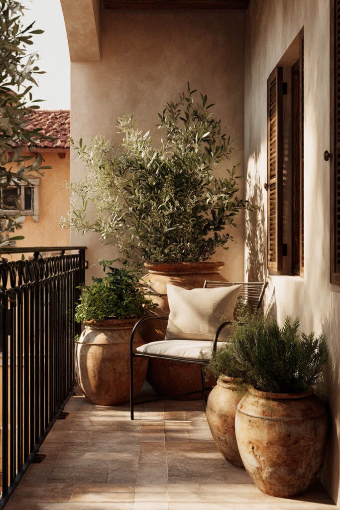 Mediterranean balcony with terracotta pots, olive tree containers, black metal chair, warm stucco walls, and layered Mediterranean plants.