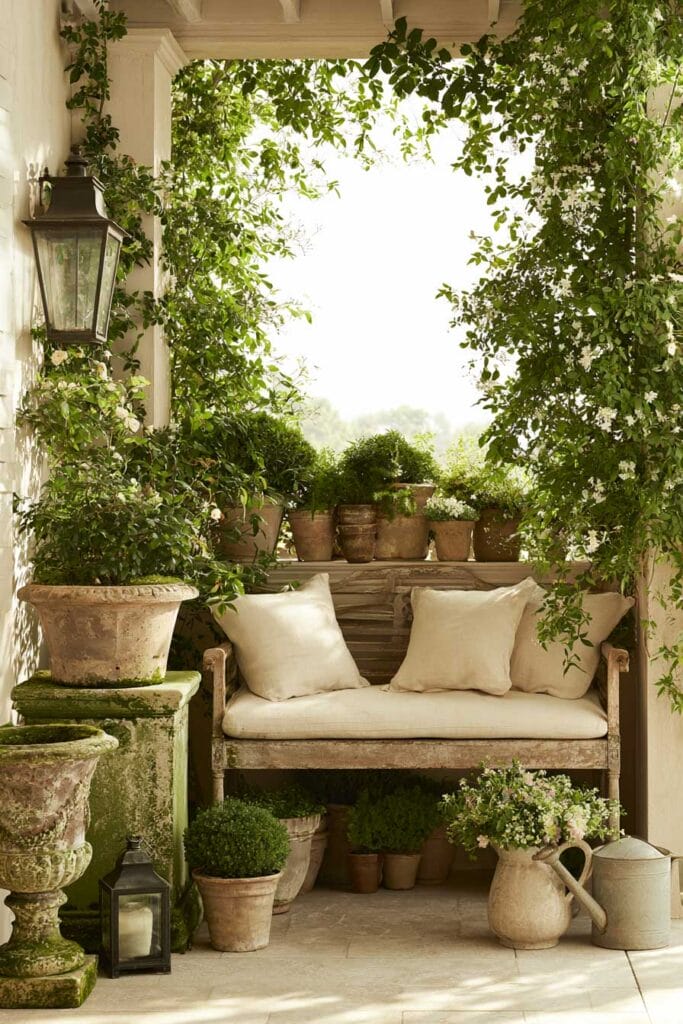 Secret garden balcony with vintage wooden bench, weathered terracotta pots, climbing jasmine, lush greenery, and European garden decor.