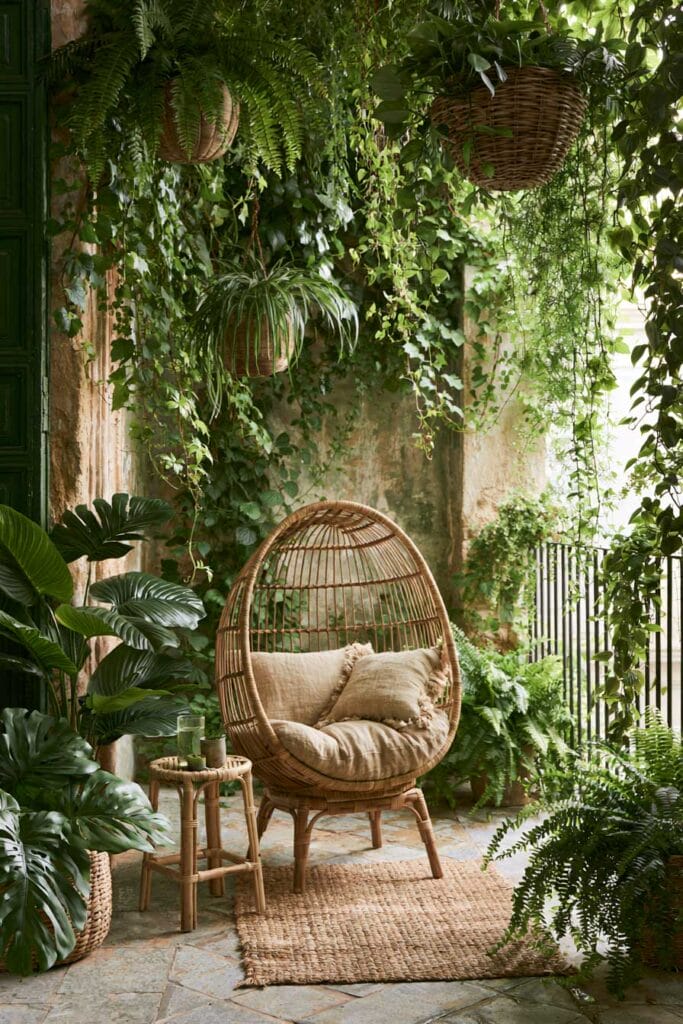 Secret garden balcony with wicker lounge chair, hanging plants, cascading vines, lush greenery, and cozy European balcony decor.