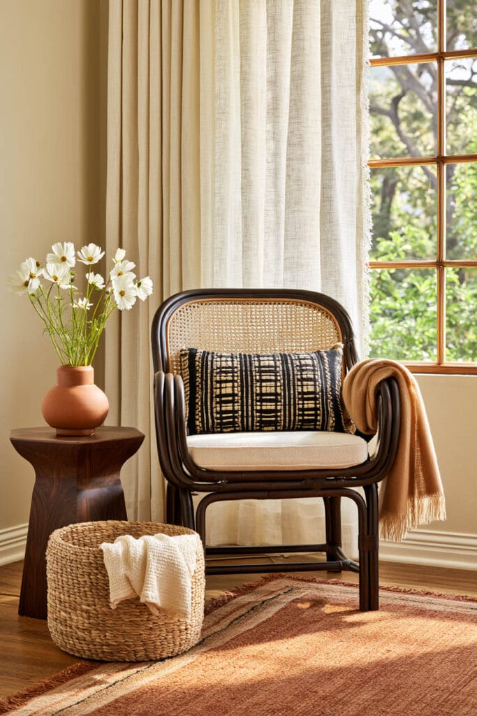 Afrohemian reading nook with woven cane chair, black and cream textile pillow, caramel throw, woven basket, wood table, and terracotta vase.